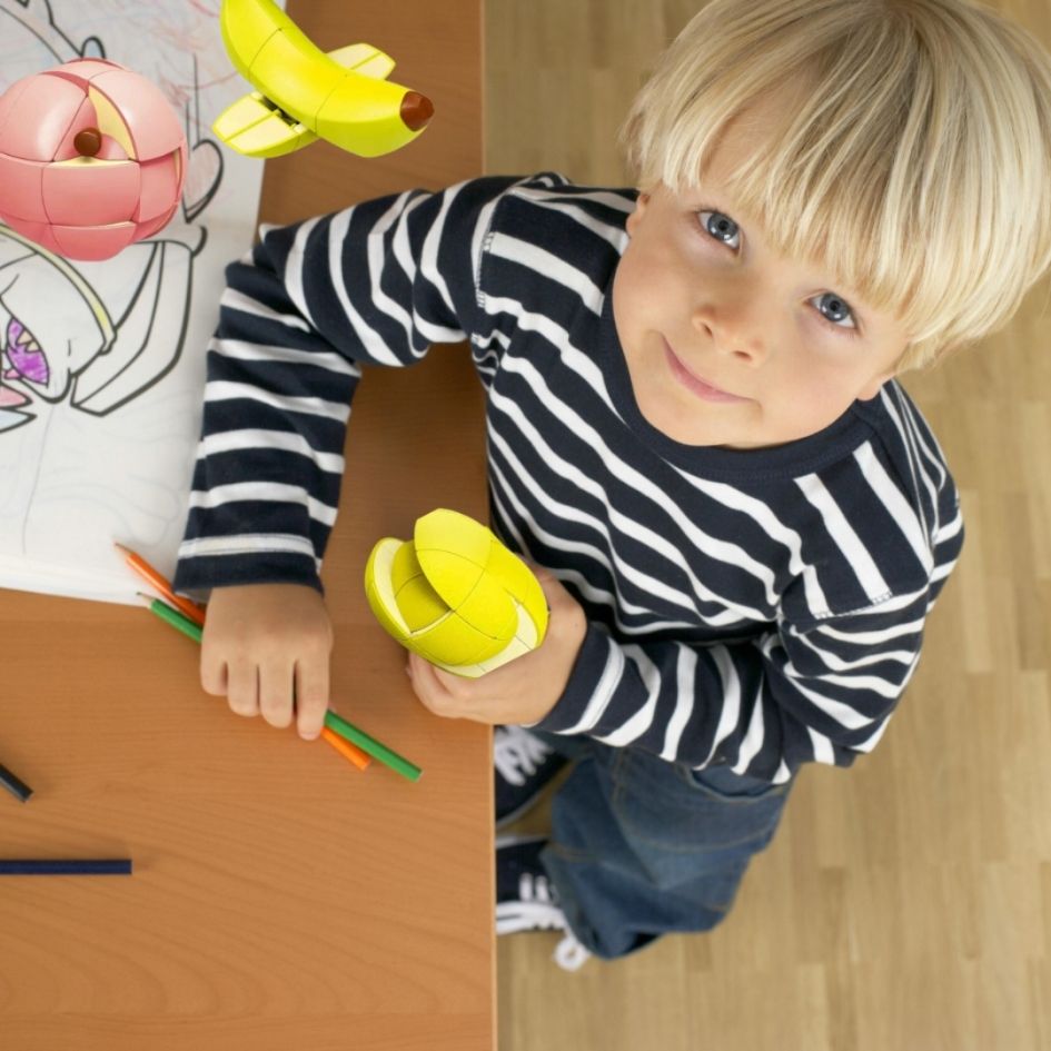 Un joli gar<con blond est assis a la table avec son puzzle 3d citron, les 2 autres rubiks cube de pomme et de banane sont russis devant lui.