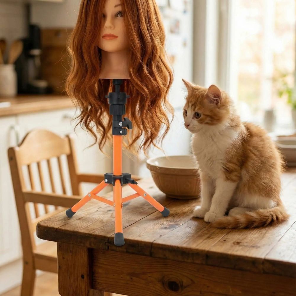 un trepied orange vif est installé sur la table de bois supportant une tete a coiffé rousse un chat adire sa nouvelle amie la tete a coiffer.