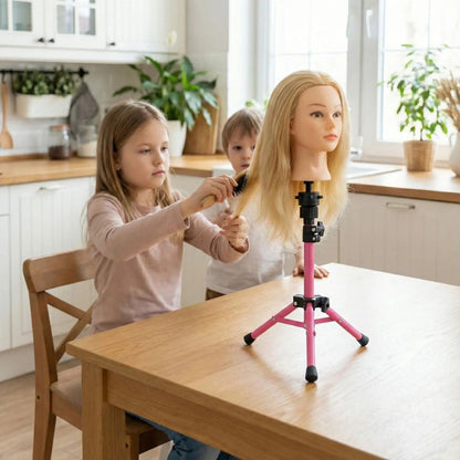 une petite fille est concentrée à pratiquer des coiffure sur sa tete a coiffer blonde juché sur son trepied de table, sur la table de la cuisine