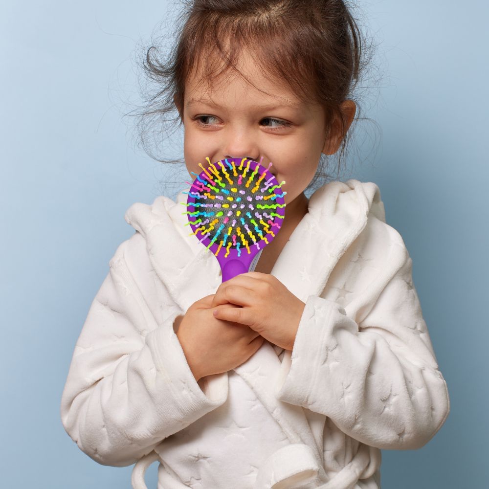 jolie fillette fière de sa brosse à cheveux aux poils multi colores arc-en-ciel et à son miroir magique inclus