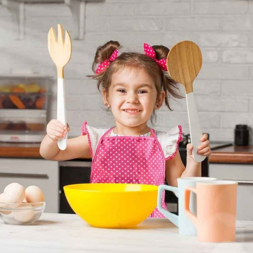 petite fille fière de faire la cuisine avec son TABLIER CUISINE ENFANT tablier de son jeu de dinet enfant rose.