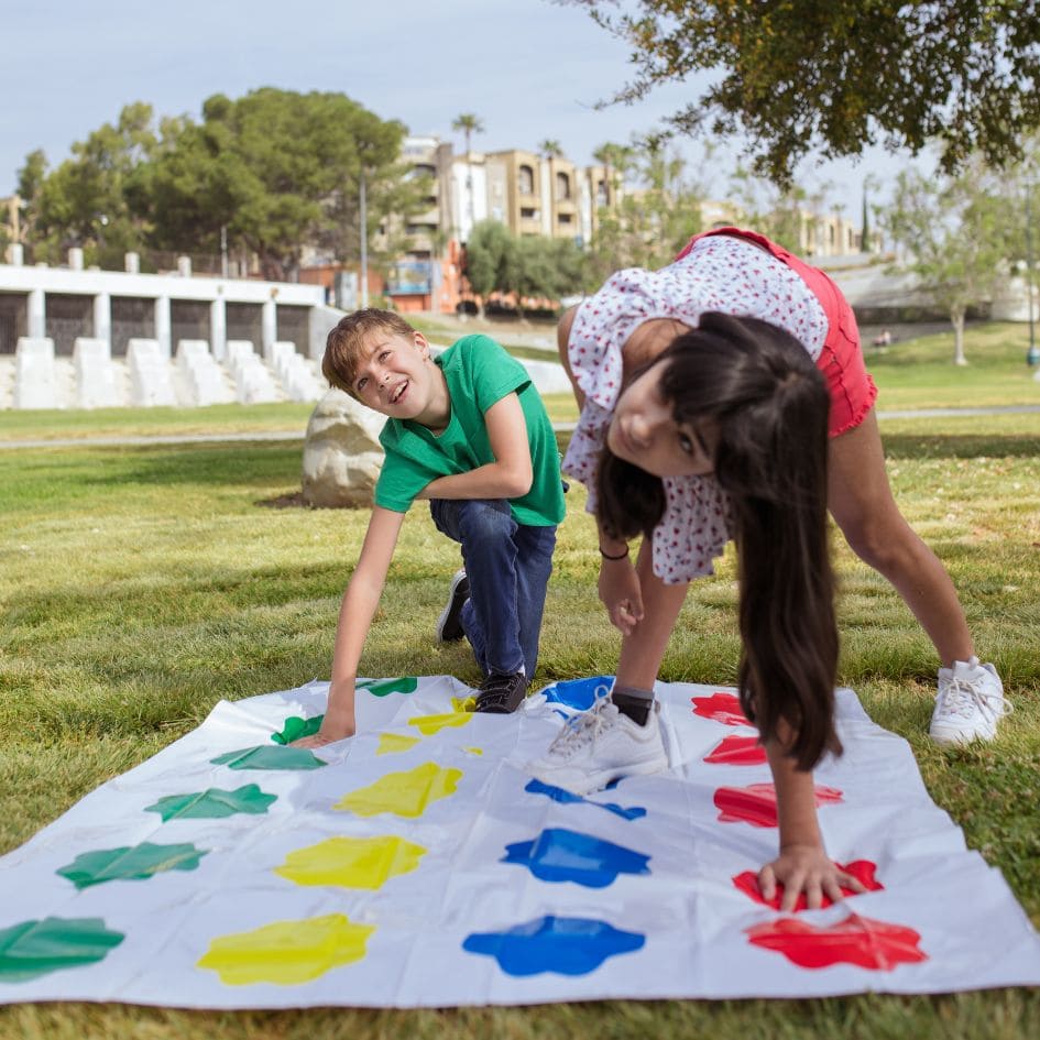 2 enfants jouent au jeu de société Twister sur la pelouse dans la cour au beau soleil