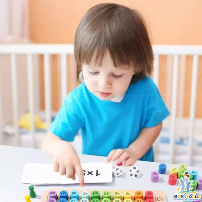 un petit garçon joue au jeu de tables de multiplication en bois avec jeton arc-en-ciel