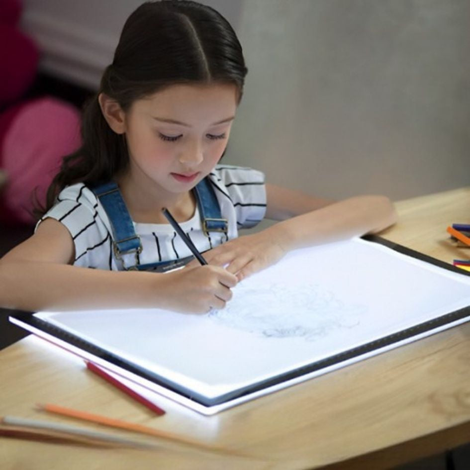 une jeune fille de 7 ans est concentrée à tracer son dessin qu'elle crée sur sa tablette lumineuse pour dessin qu'elle a reçu du Père Noël