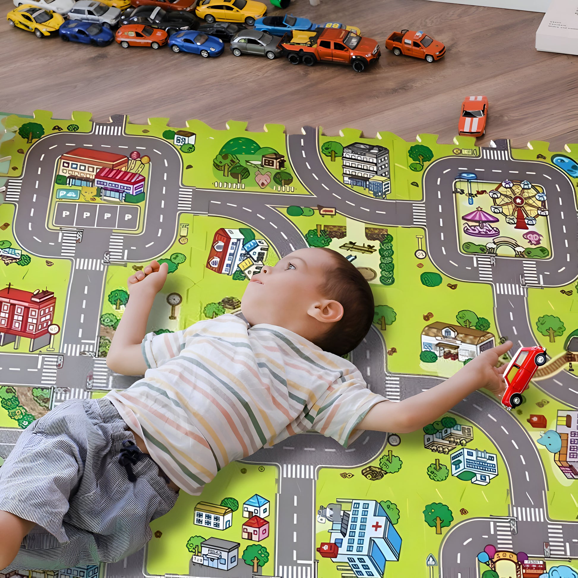 un gamin de 3 ans est couché sur son tapis circuit voiture confortable il fait rouler ses voiture dans les routes dessinées