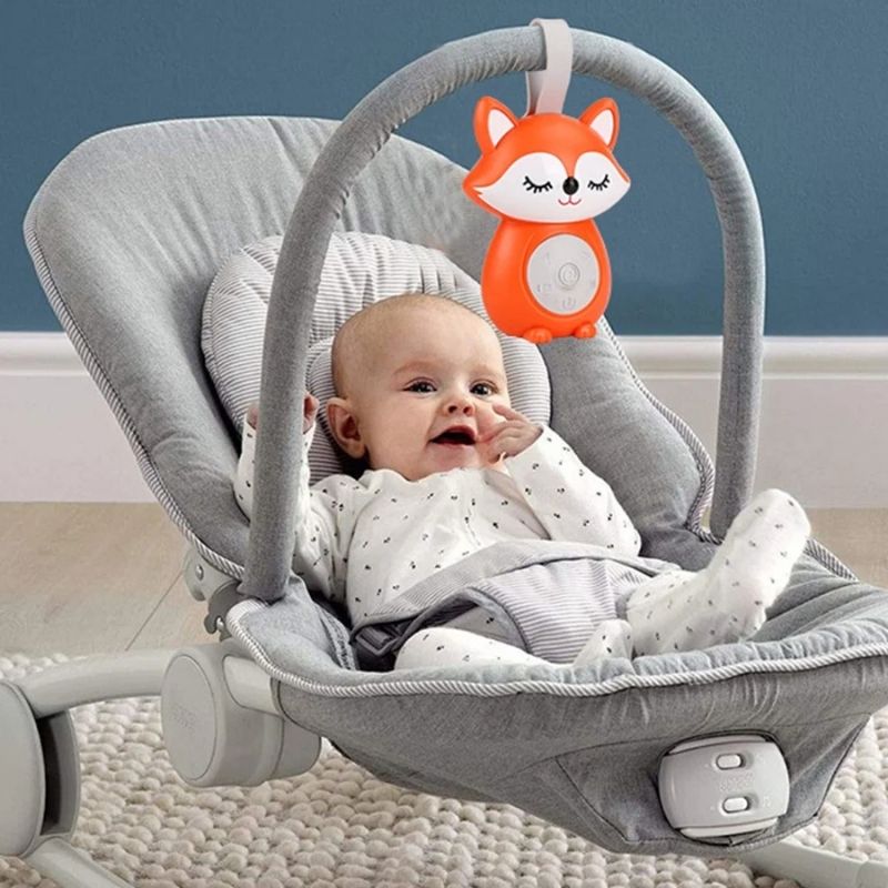 un bébé de 6 mois dans sa coquille de voyage écoute sa musique  avec sa Veilleuse bruit blanc renardeau orange douceur